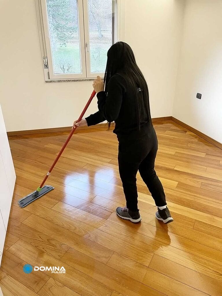 Una donna che pulisce un pavimento di legno con uno straccio.