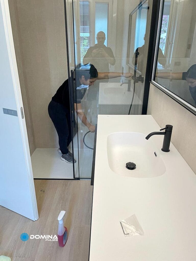 Un uomo pulisce un bagno con una doccia in vetro in un appartamento post ristrutturazione a Legnano.