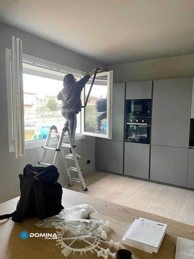 Ua donna che lavora su una scala in cucina per le pulizie post cantiere in un appartamento a Legnano.