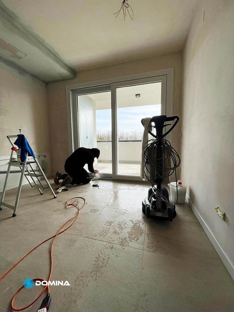 Una donna inginocchiata vicino ad una porta a vetri in provincia di Monza Brianza per la pulizia dei vetri delle finestre.