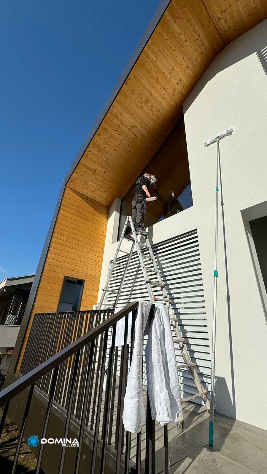 Un uomo su una scala pulisce le finestre di una casa per farle brillare dopo essere state ristrutturate con l'aiuto di Domina Pulizie.