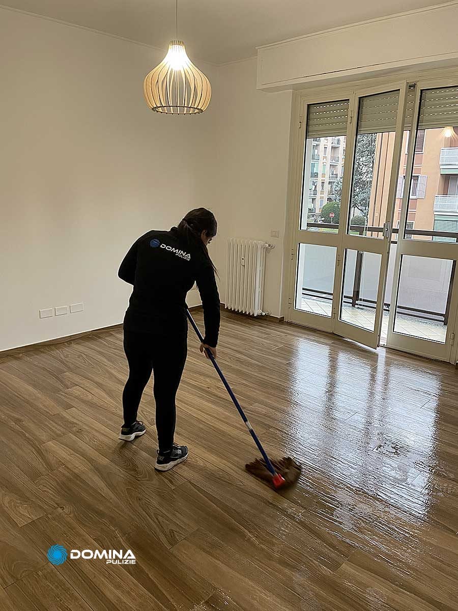 Una donna che pulisce un pavimento di legno in una stanza vuota dopo la ristrutturazione.