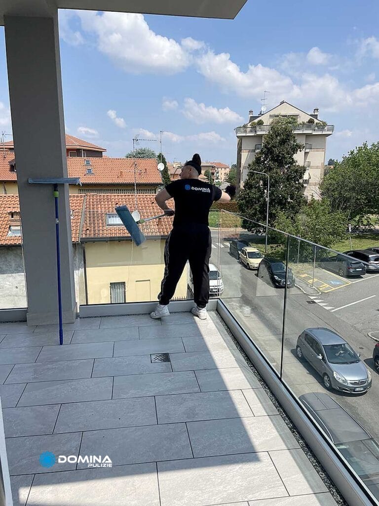 Una donna dell'azienda "Domina Pulizie" pulisce un balcone in vetro dopo la ristrutturazione.