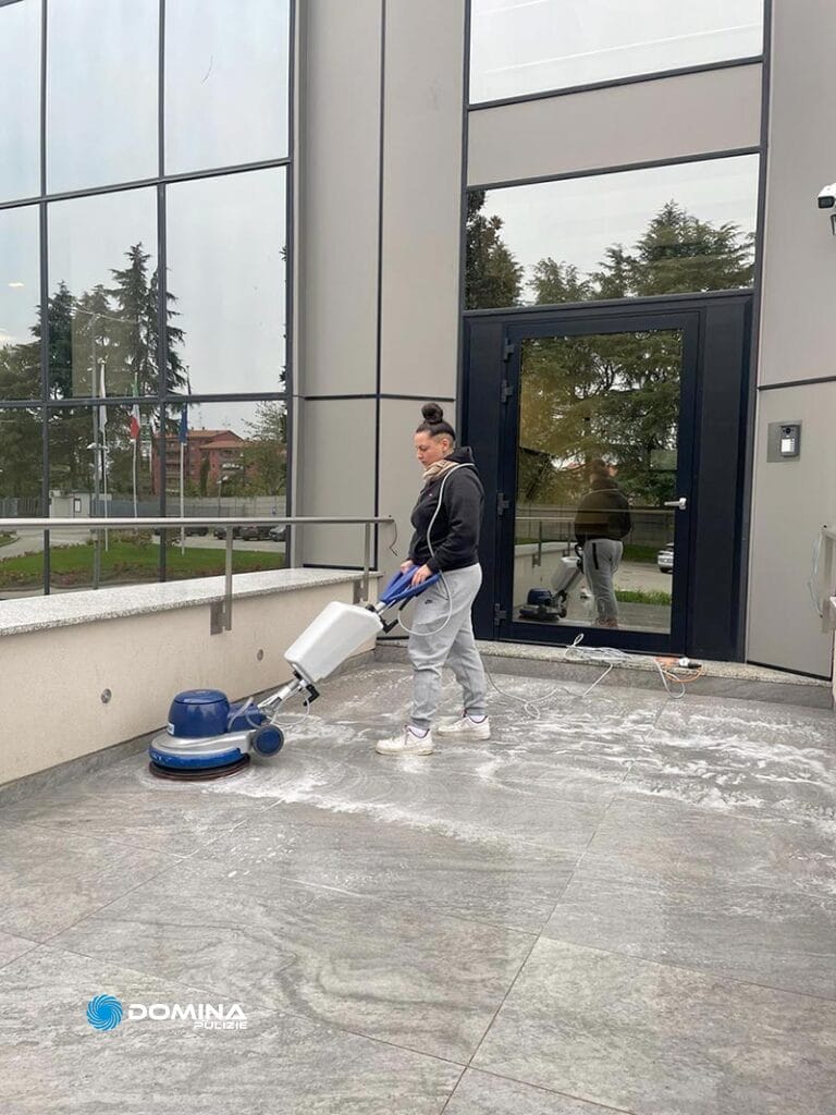 Una donna che pulisce un pavimento di cemento davanti a un edificio.