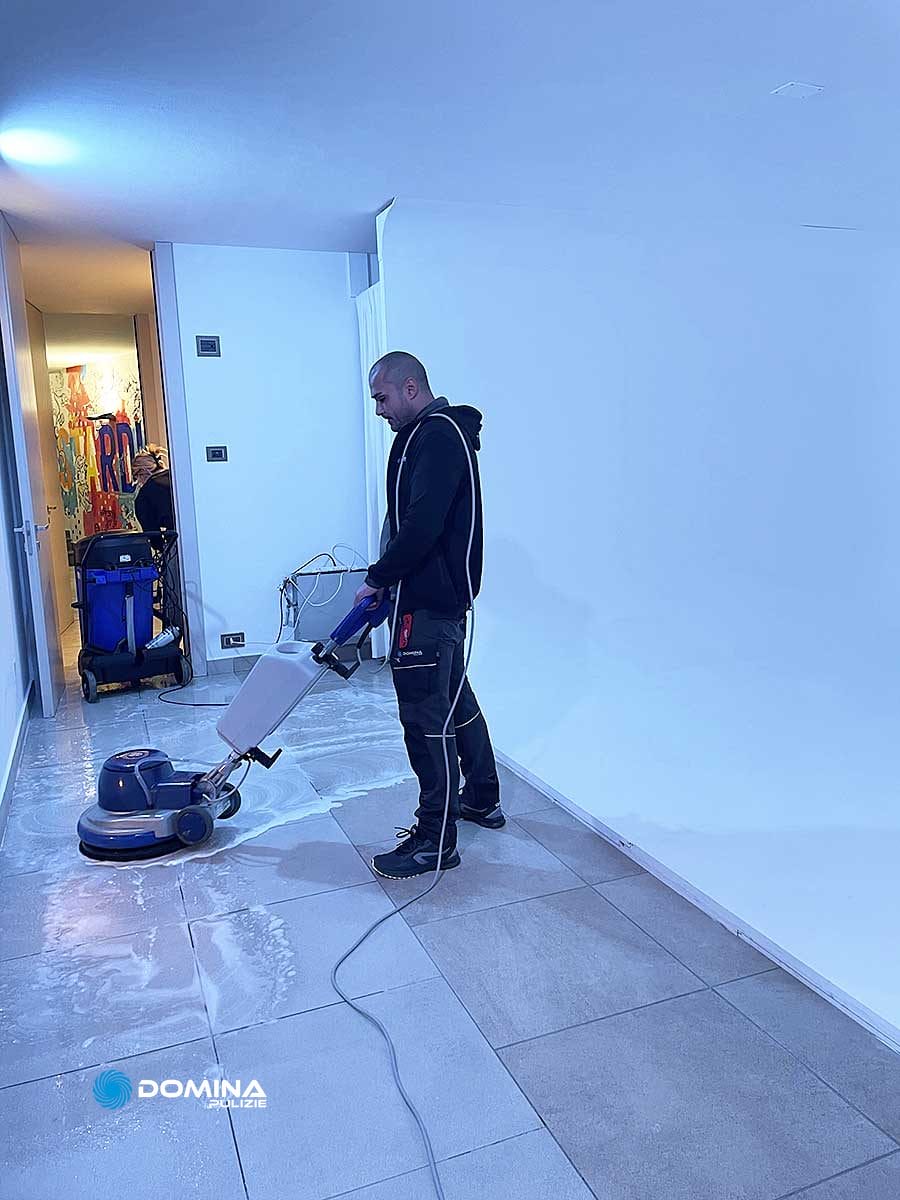 Un uomo di Domina Pulizie esegue una pulizia professionale di un pavimento con una monospazzola.
