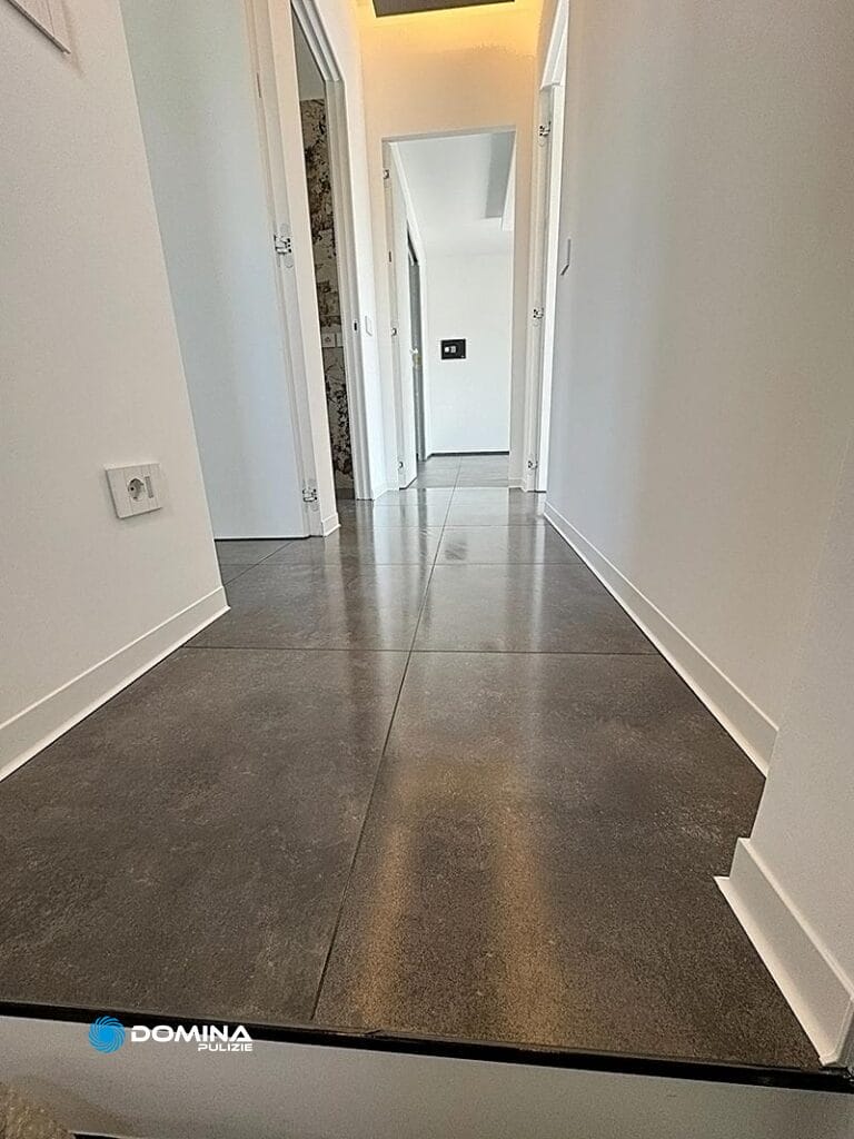 Un corridoio con pavimento piastrellato grigio, pareti bianche e porte multiple, visto da un angolo basso, mantenuto in modo impeccabile da "pulizie appartamenti Rescaldina.
