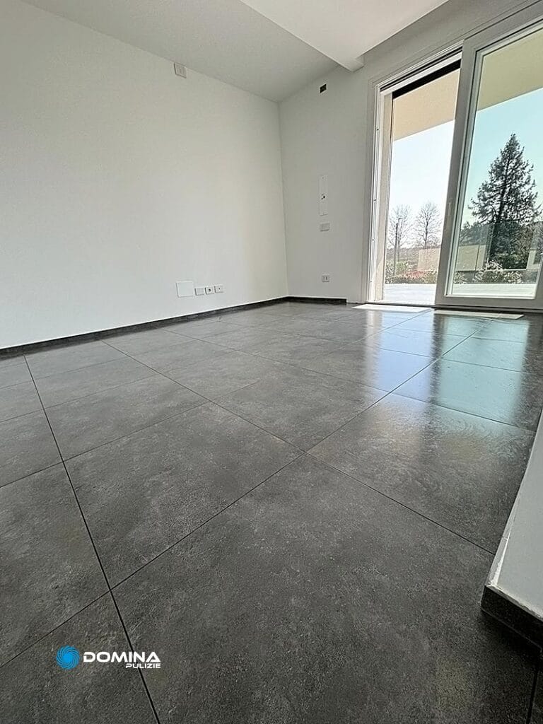 Stanza vuota con pavimento piastrellato grigio e pareti bianche vicino ad una grande finestra, pulita da un'impresa professionale di pulizie rescaldina.
