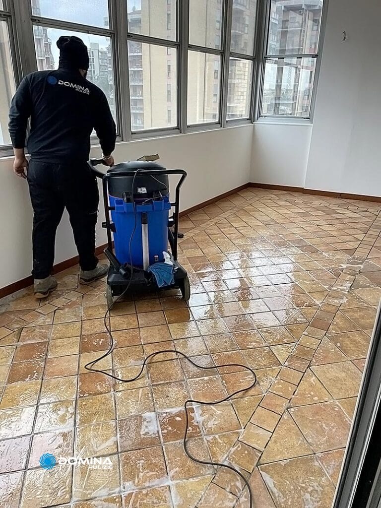 Persona che pulisce un pavimento piastrellato con un aspirapolvere industriale in una stanza vuota a Cernusco sul Naviglio.