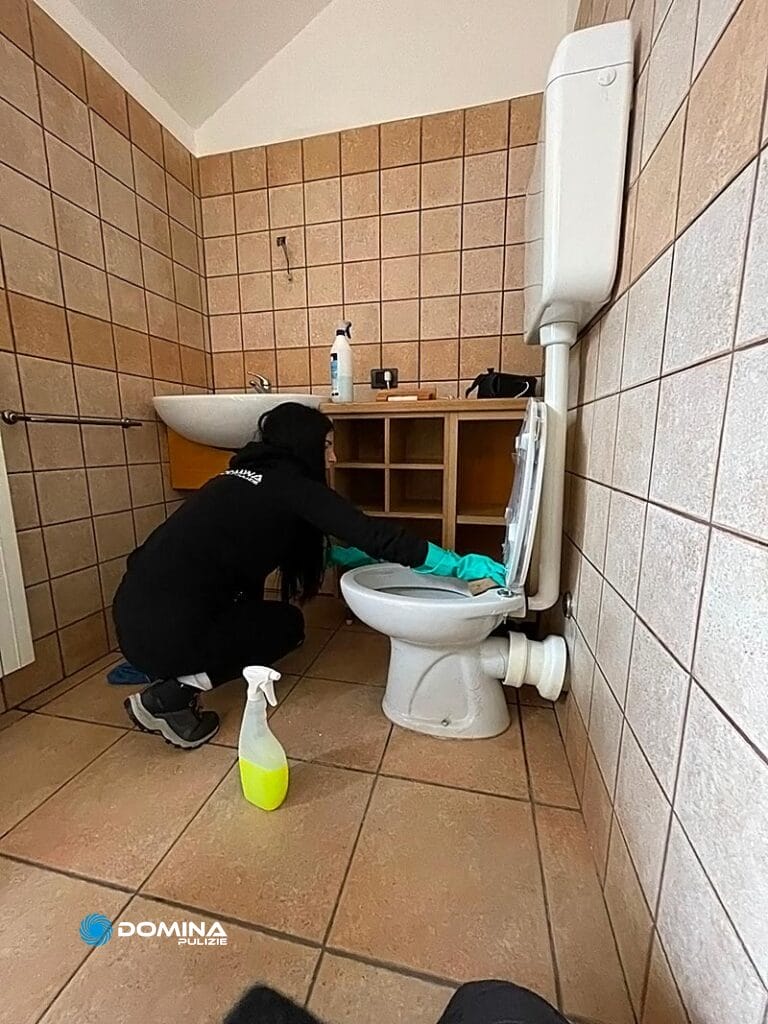 Persona che effettua le pulizie post ristrutturazione Senago pulisce una toilette in un bagno piastrellato.