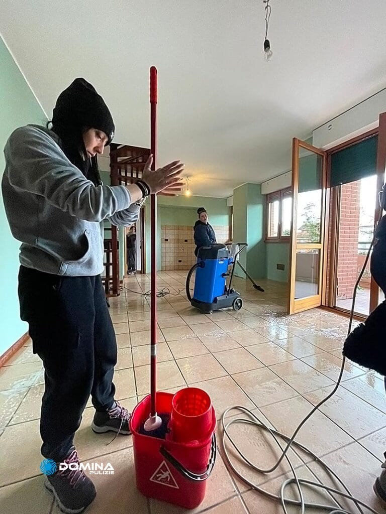 Persona che si prepara a pulire una stanza con un'altra persona che utilizza attrezzature per la pulizia sullo sfondo per le pulizie post ristrutturazione Senago.