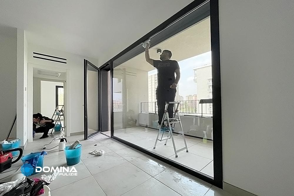 Una persona di Domina Pulizie in piedi su una scala a pioli pulisce un serramento in una stanza per le pulizie dopo la ristrutturazione.