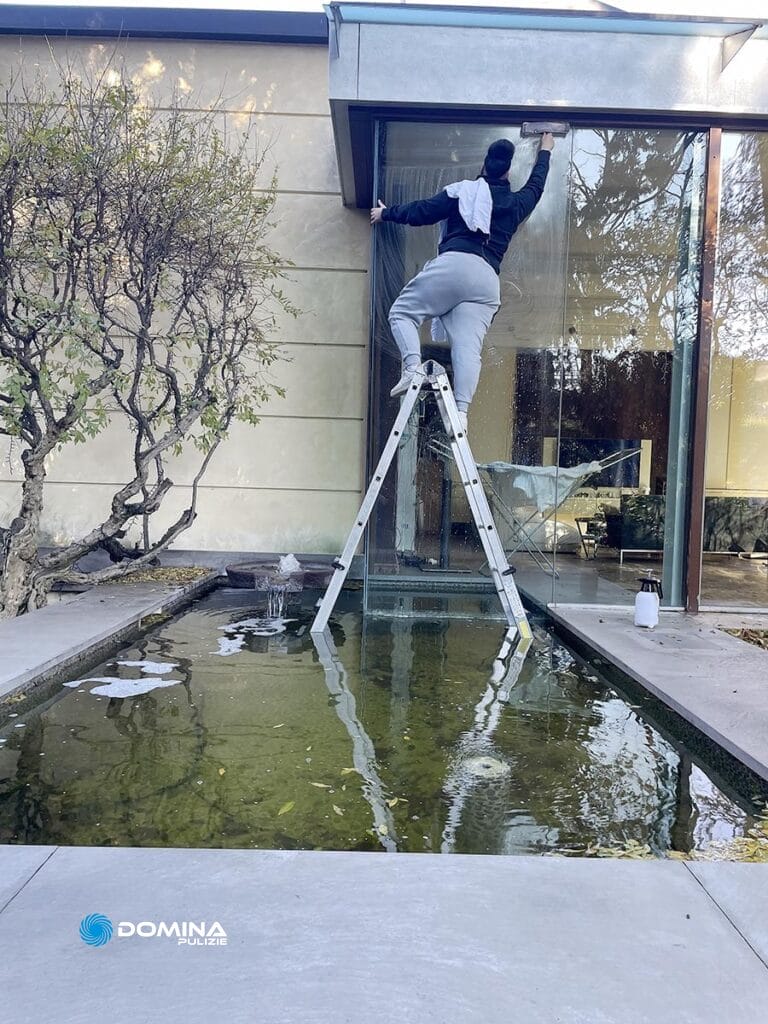 Una persona in tenuta da lavoro in piedi su una scala mentre pulisce delle vetrate all'esterno di un edificio per Impresa di Pulizie a Monza.