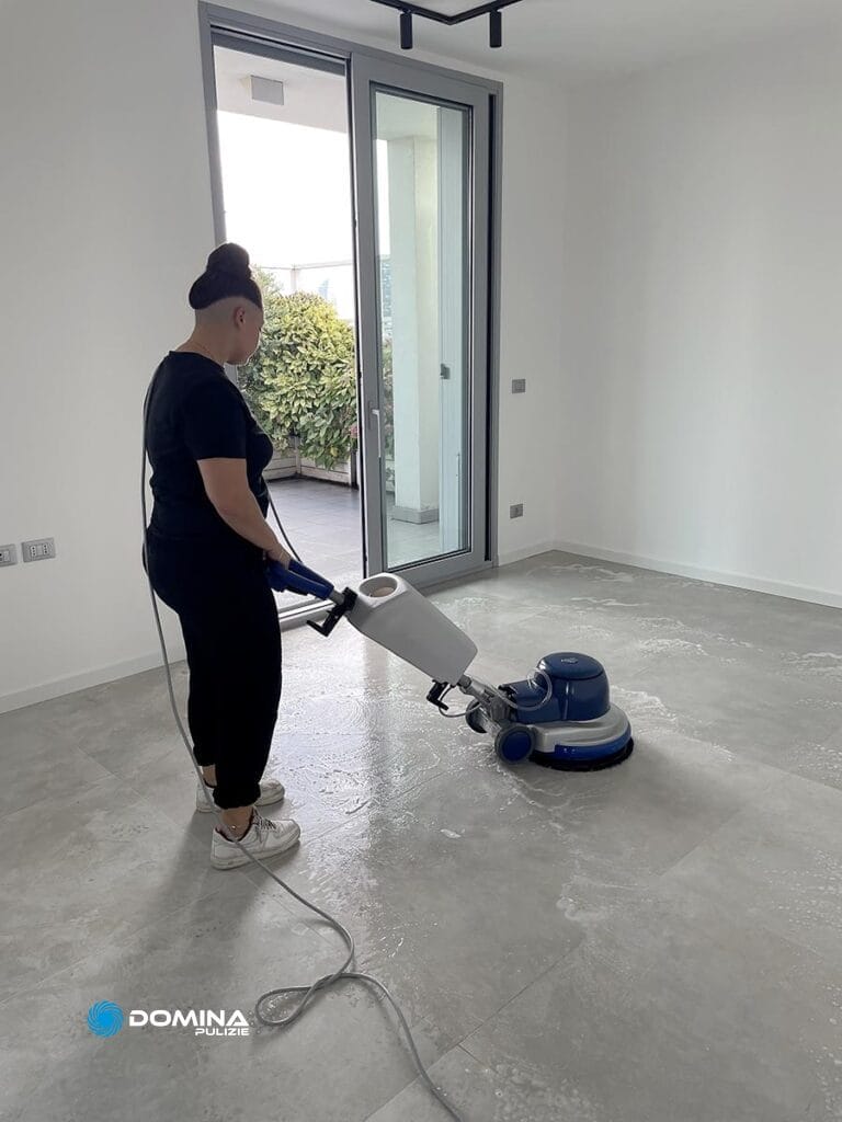 Persona che utilizza una macchina lucidatrice per pulire o lucidare una grande stanza vuota con pavimento piastrellato presso l'Impresa di Pulizie a Monza.