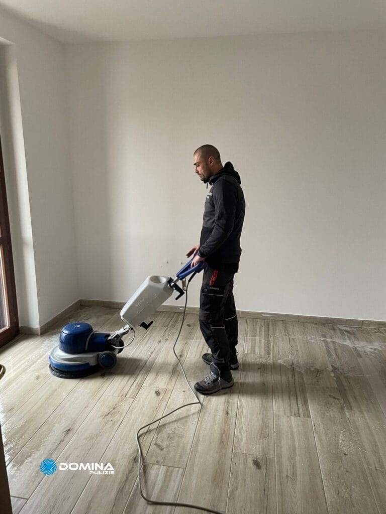 Un uomo che utilizza un lucidatore per pulire o lucidare un pavimento in legno all'interno di una stanza vuota in una casa sottoposta a Pulizie post ristrutturazione.