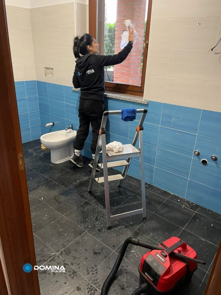 Persona che pulisce lo specchio del bagno mentre si trova su una scala a pioli dopo una pulizia post-ristrutturazione.
