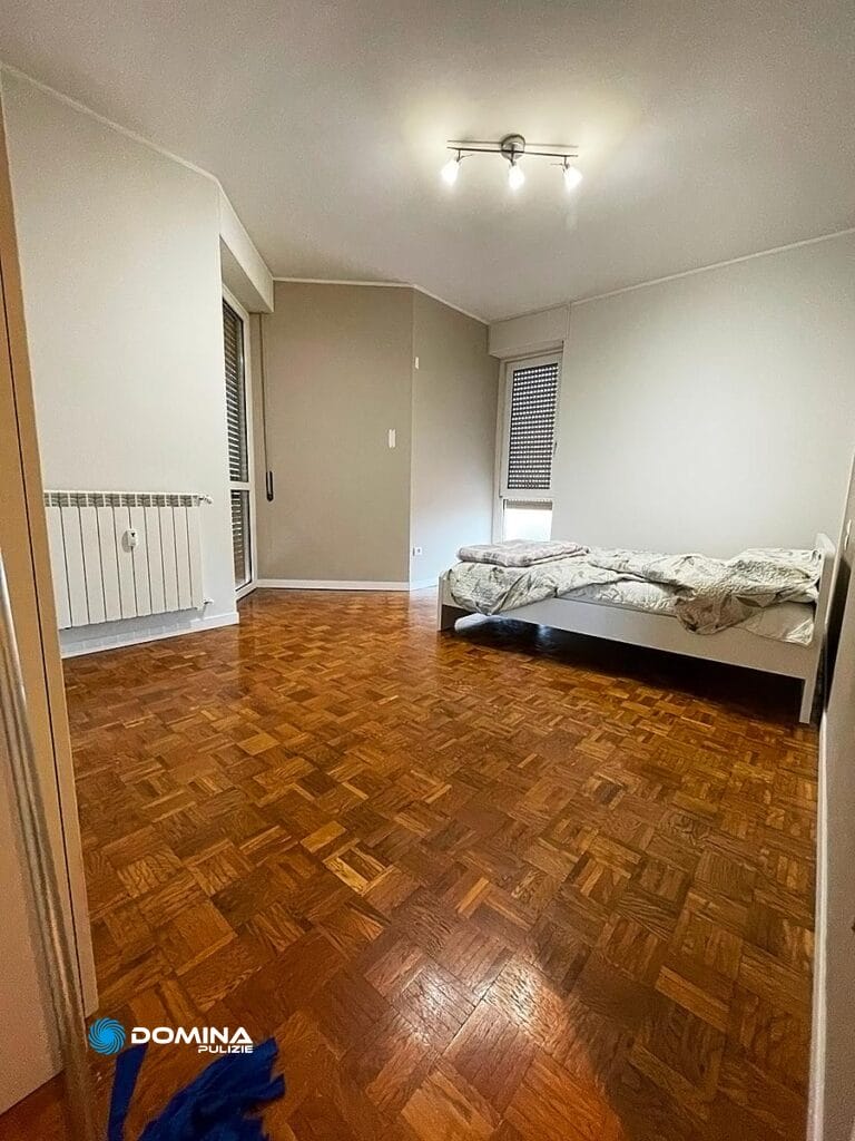 Una stanza arredata in modo spartano con pavimento in parquet, caratterizzata da un letto singolo e decorazioni minimali, curata dall'impresa di pulizie