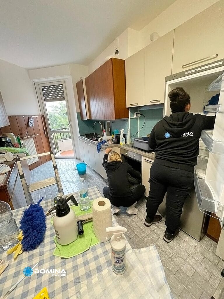 Due individui dell'impresa di pulizie a Olgiate Olona stanno pulendo una cucina, con una persona che pulisce il frigorifero e l'altra