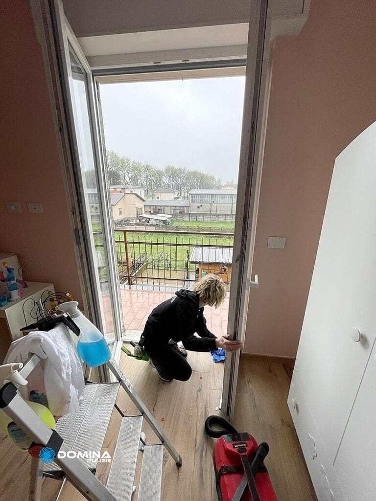 Persona di Domina Pulizie che pulisce il pavimento di una stanza con la porta del balcone aperta.