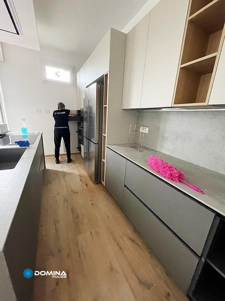 Una persona in piedi in una cucina moderna con pavimento in legno e mobili grigi, pulita da Domina Pulizie.