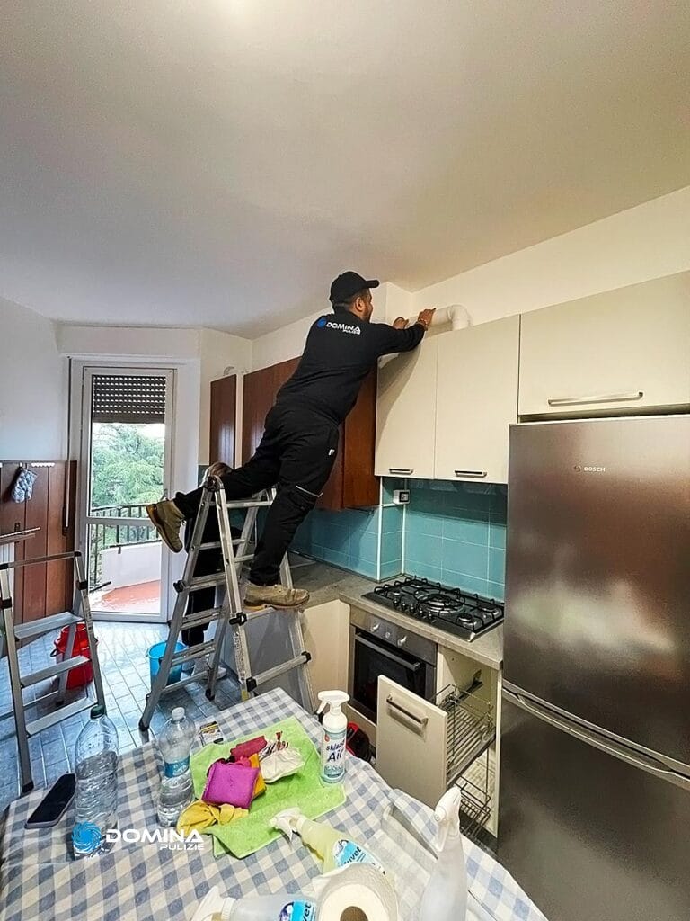 Una persona in piedi su una scala a pioli per pulire i mobili di una cucina per un appartamento a Olgiate Olona.