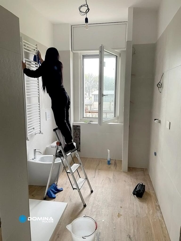 Persona su una scala a pioli che pulisce un muro in una stanza dopo la ristrutturazione, seguita da una pulizia completa dell'appartamento post-ristrutturazione da parte di Domina Pulizie.