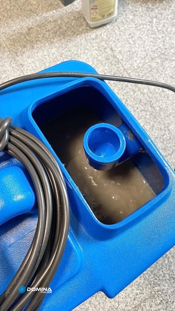 Un contenitore di plastica blu con un tubo a spirale e un liquido, probabilmente utilizzato per scaricare o trasferire fluidi nel processo di lavaggio divani di Domina Pulizie.