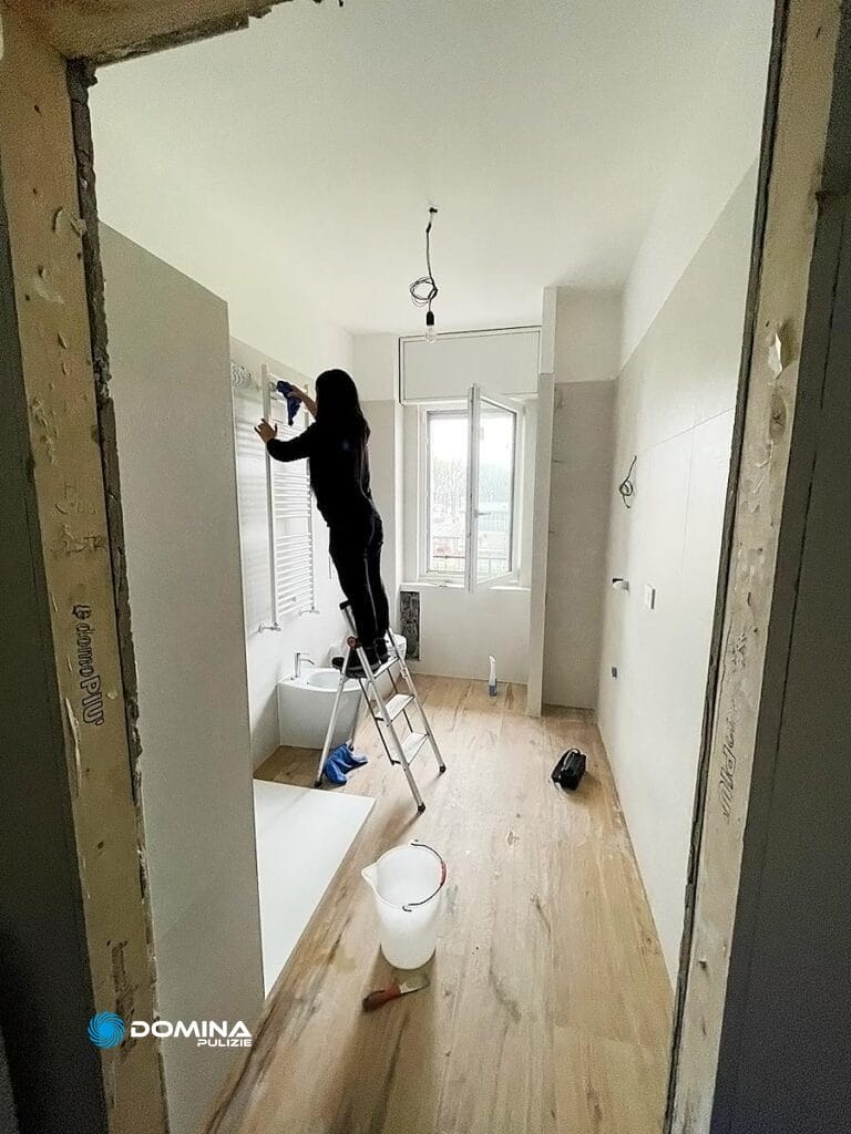 Persona su una scala a pioli che pulisce un muro in una stanza dopo la ristrutturazione, seguita da una pulizia completa dell'appartamento post-ristrutturazione da parte di Domina Pulizie.
