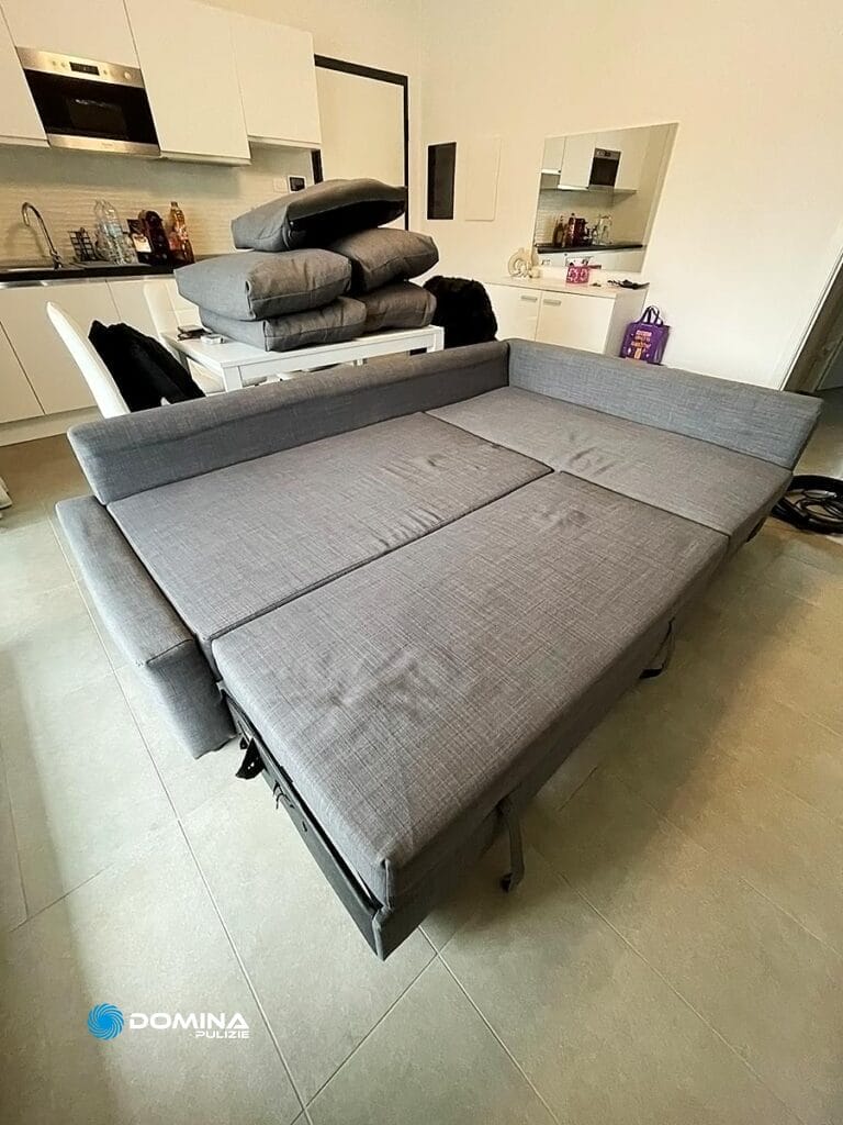 Un divano componibile grigio trasformato in letto in un salotto moderno di Domina Pulizie.