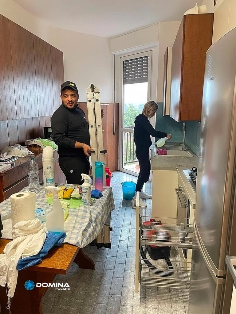 Un uomo e una donna di un'impresa di pulizie a Olgiate Olona puliscono e riordinano una cucina con prodotti per la pulizia e una scala presenti.