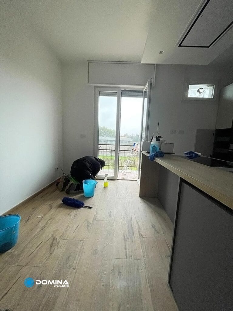 Persona che pulisce il pavimento di una cucina moderna con straccio e secchio per Domina Pulizie.