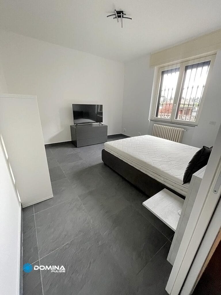Camera da letto minimalista con letto, comodino e televisione, mantenuta in maniera impeccabile da Domina Pulizie.