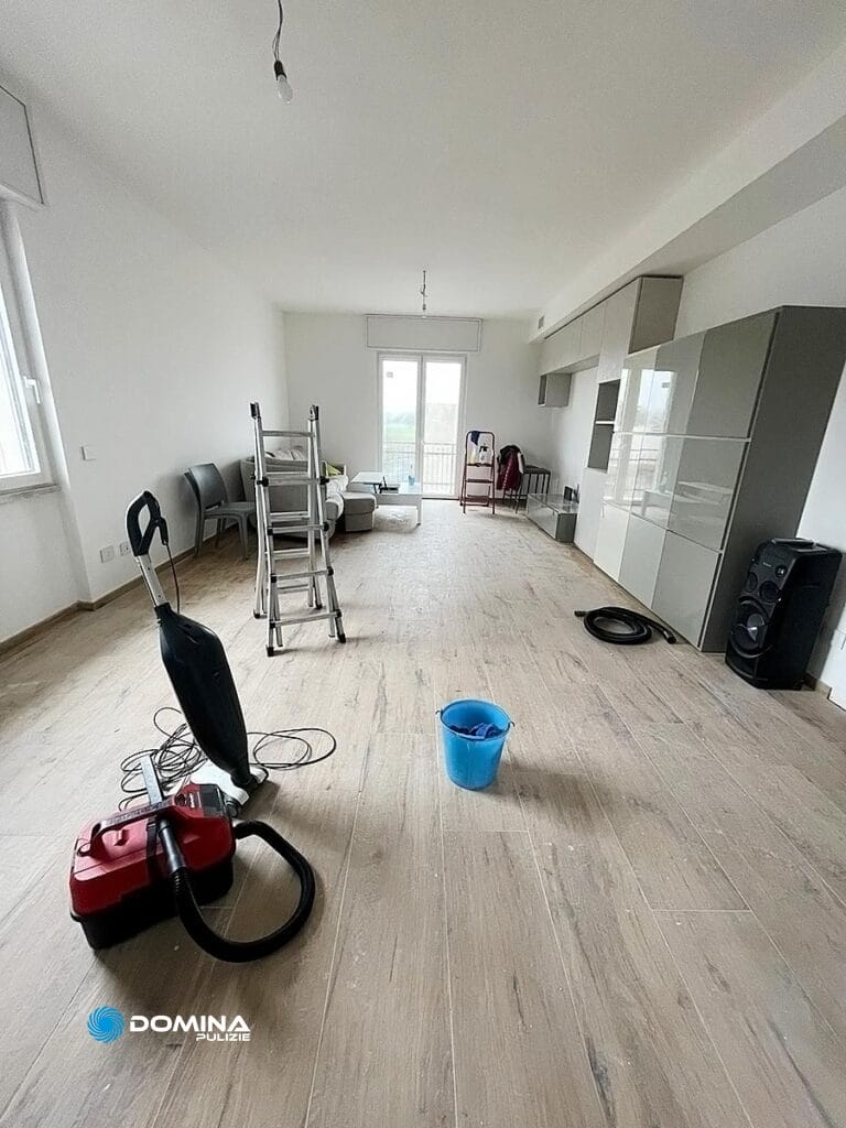 Una stanza non ammobiliata in fase di pulizia, gestita da Domina Pulizie, con presente aspirapolvere, secchio e scala.
