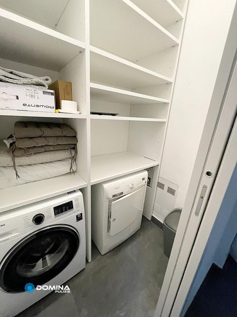 Un ordinato ripostiglio lavanderia con lavatrice, asciugatrice, ripiani e oggetti per riporre gli oggetti, mantenuto in modo impeccabile da Domina Pulizie.