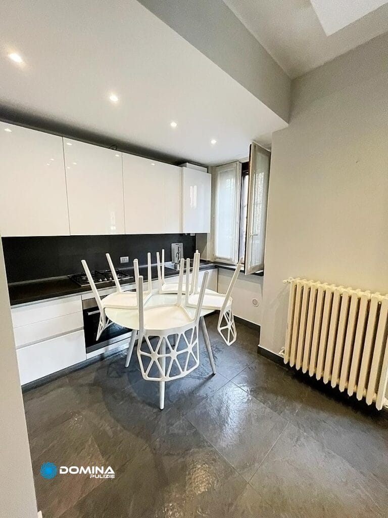 Cucina moderna con mobili bianchi, alzatina nera, tavolo da pranzo e un classico radiatore vicino alla finestra, gestita da Domina Pulizie.
