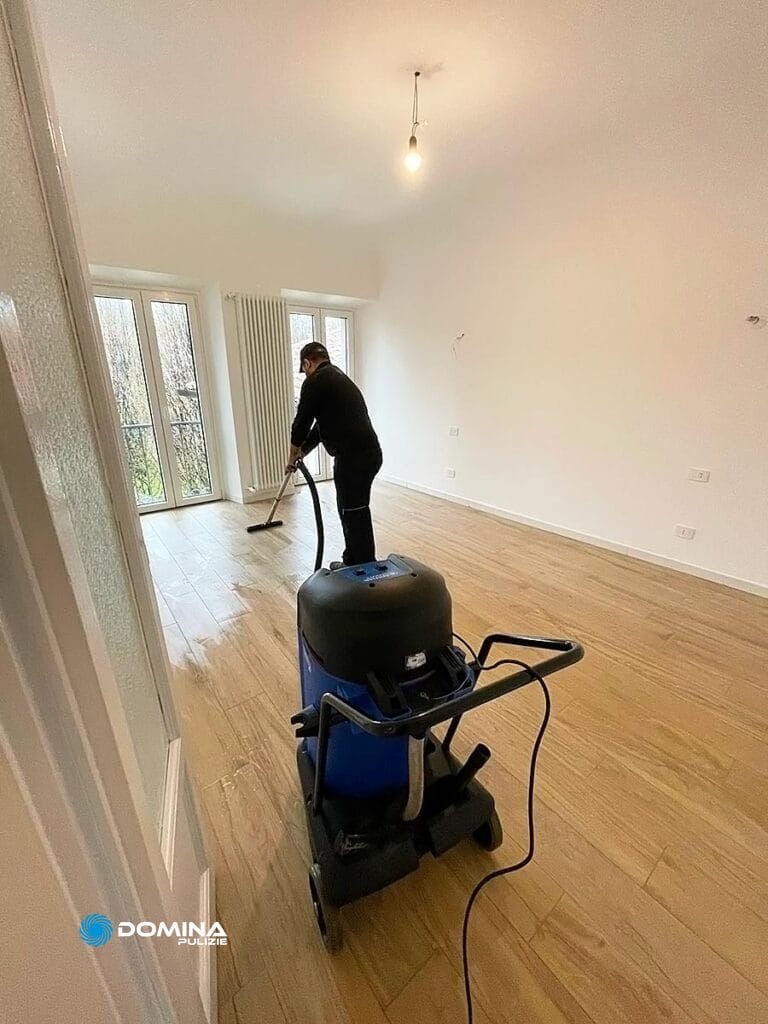 Persona che pulisce una stanza vuota con un aspiratore professionale per pavimenti di Domina Pulizie.