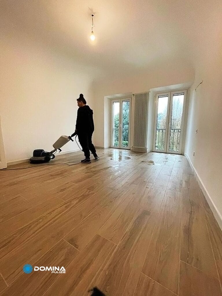Una persona utilizza una lucidatrice per pavimenti in un'ampia stanza vuota con pavimenti in legno, facendo parte dell'impresa di pulizie a Bollate