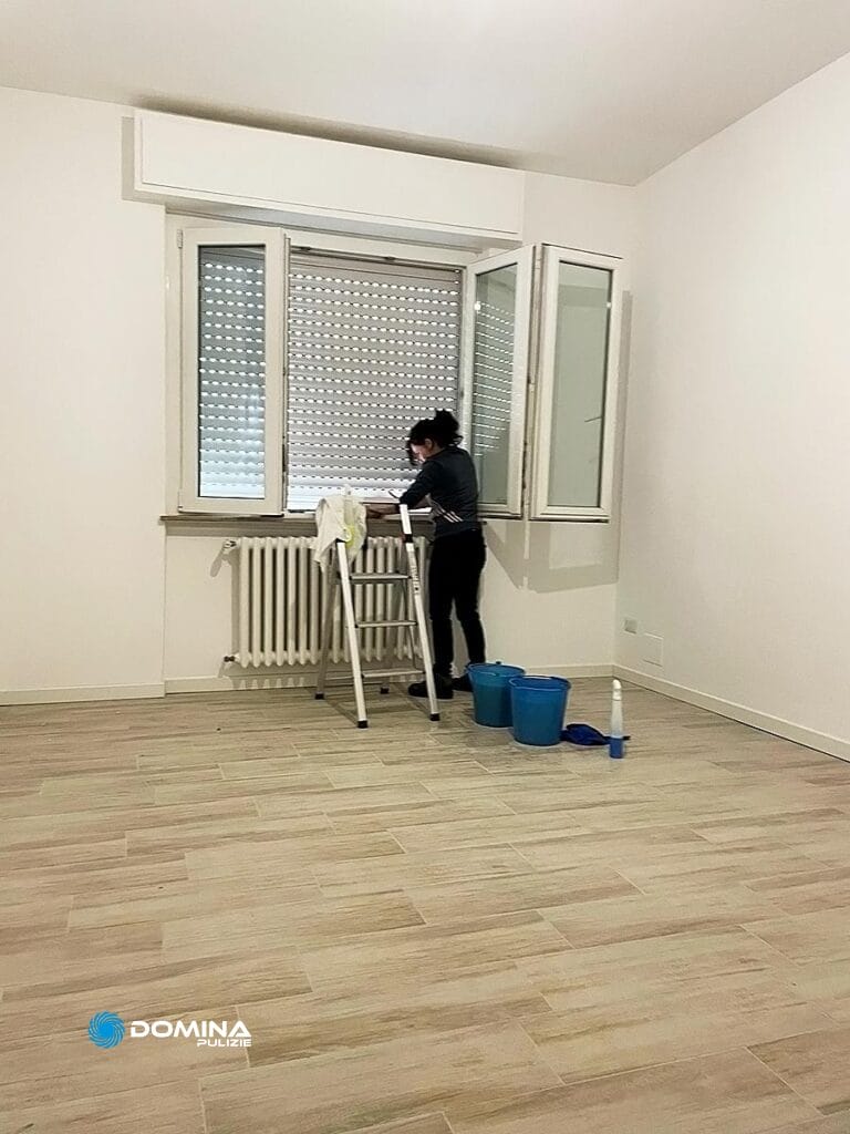 Una persona che esegue una "pulizia post cantiere Milano" in una stanza con uno spazzolone e un secchio vicino a una finestra con le persiane aperte per Domina Pulizie.