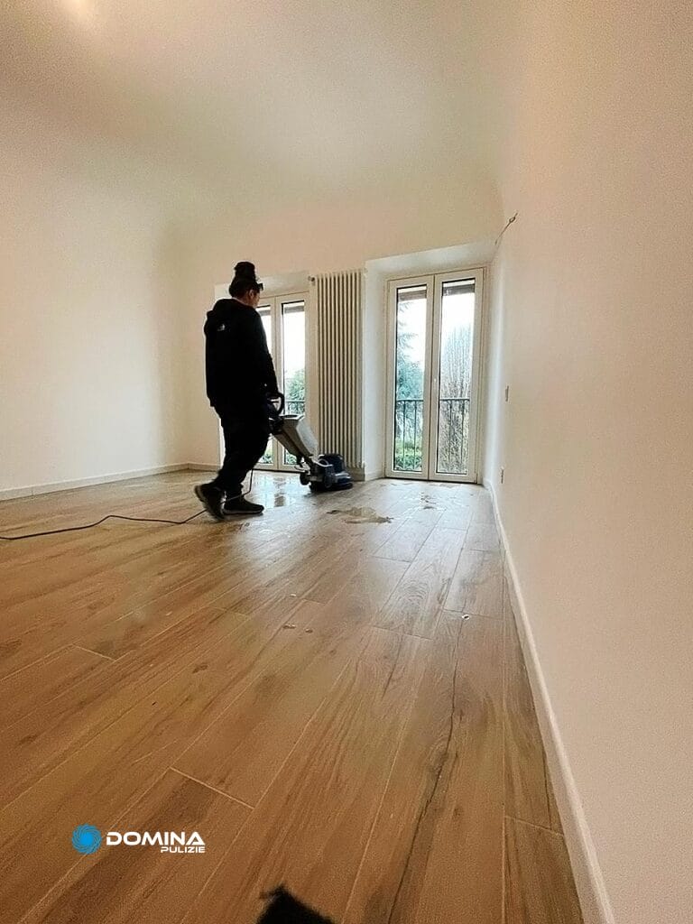 Una persona in piedi in una stanza vuota con pavimento in legno, guardando verso la porta di un balcone, dopo che la "Domina Pulizie", un'impresa di pulizie a Bollate, ha completato il suo lavoro