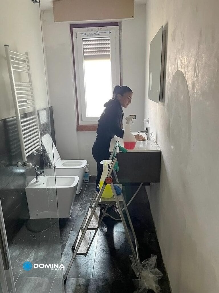Una persona in piedi su una scala effettua pulizie appartamento post cantiere a Villa Guardia, pulendo un lavandino del bagno.