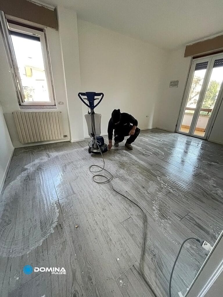 Una persona sta pulendo un pavimento grigio con l'aspirapolvere in una stanza non ammobiliata per Domina Pulizie durante le pulizie appartamento post cantiere a Villa Guardia.