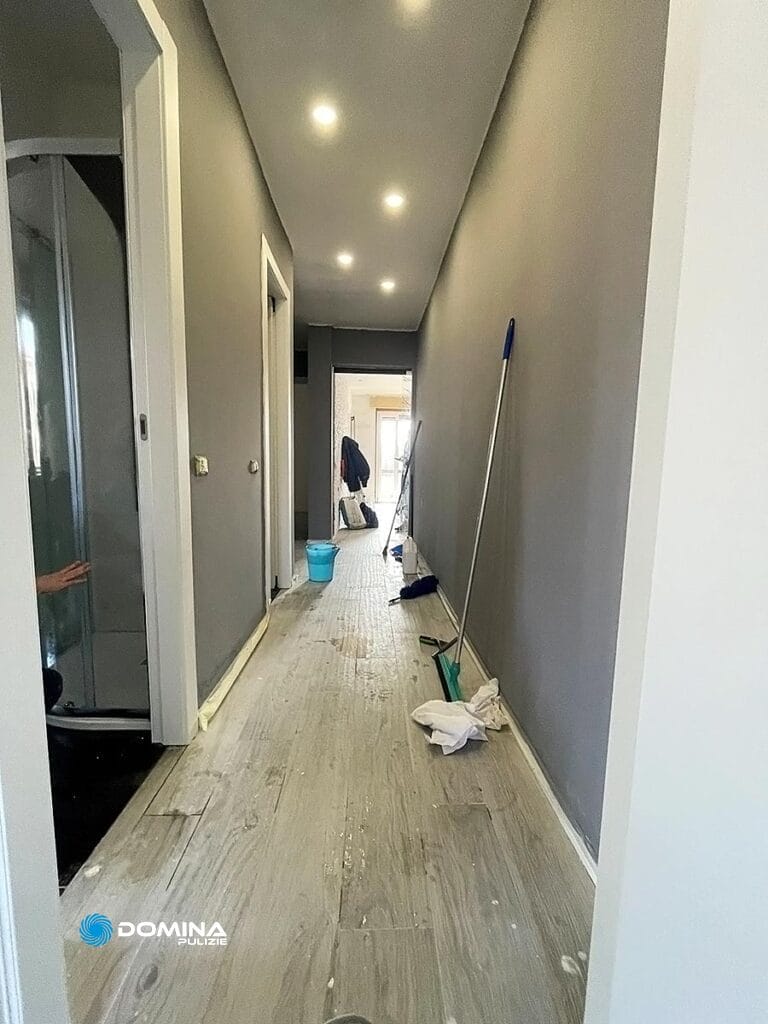 Un corridoio nel bel mezzo delle pulizie di Domina Pulizie, con spazzoloni, secchi e panni sparsi sul pavimento del cantiere a Villa Guardia.