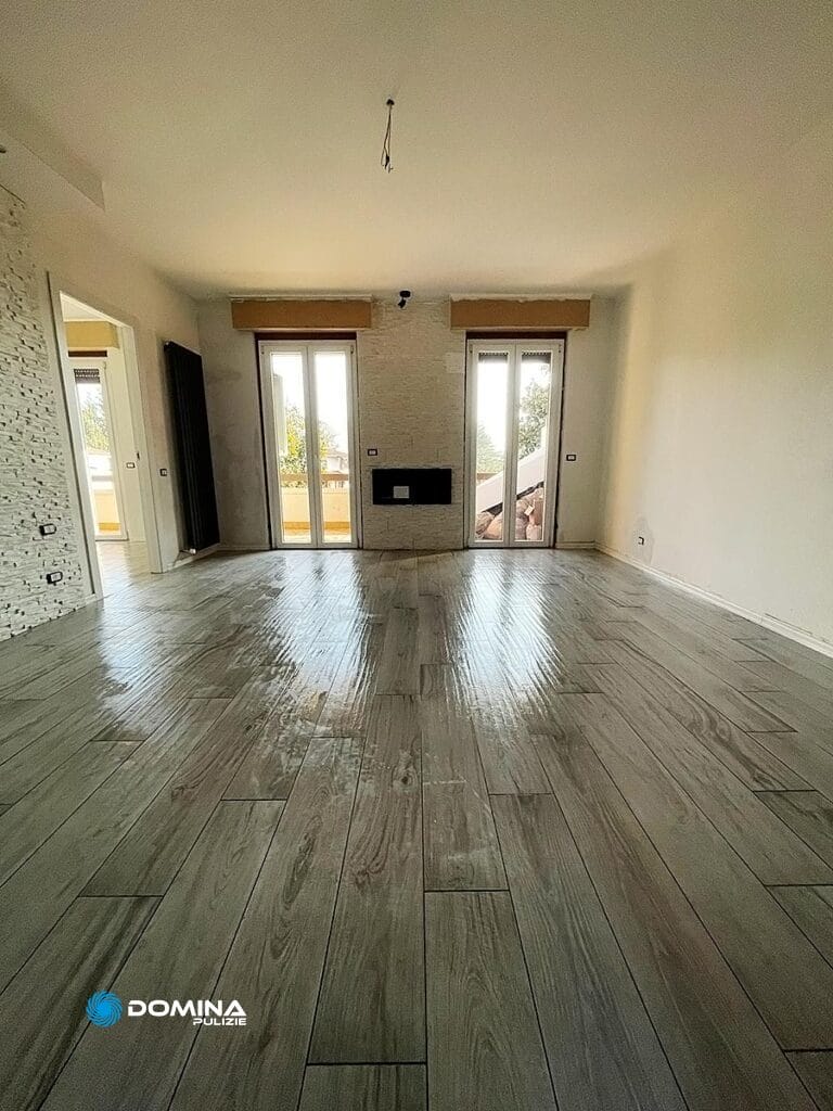 Camera non ammobiliata con pavimento in piastrelle grigie con motivi in legno e pareti in mattoni bianchi con caminetto, in attesa delle pulizie appartamento post cantiere a Villa Guardia.