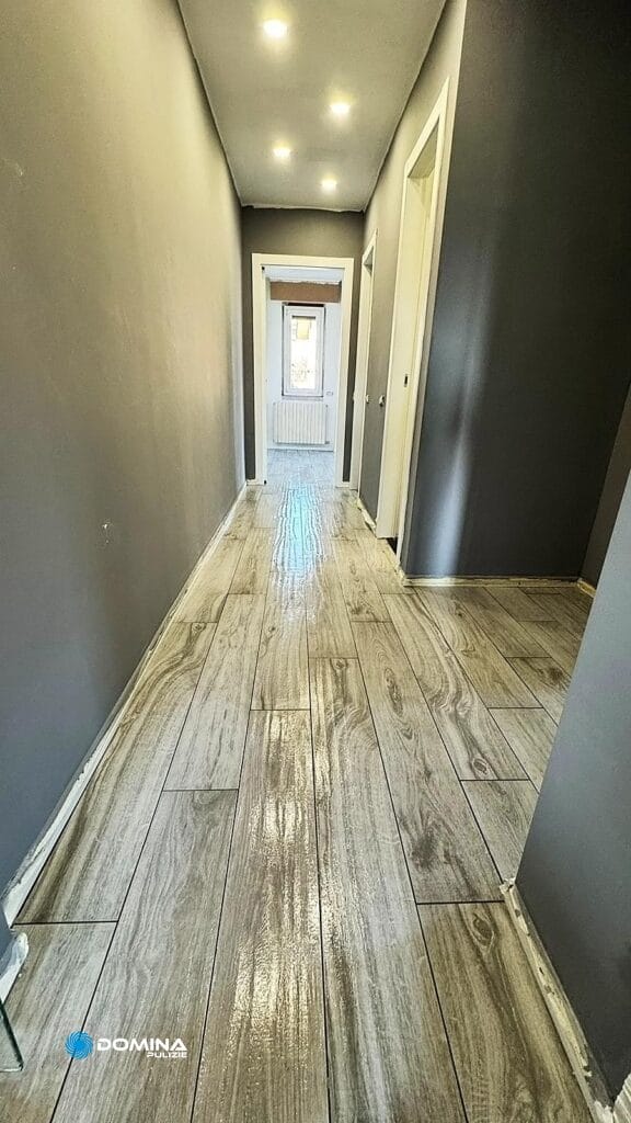 Uno stretto corridoio con pavimento grigio effetto legno conduce in fondo ad una stanza molto luminosa, appena mantenuta secondo le "pulizie appartamento post cantiere" di Villa Guardia.