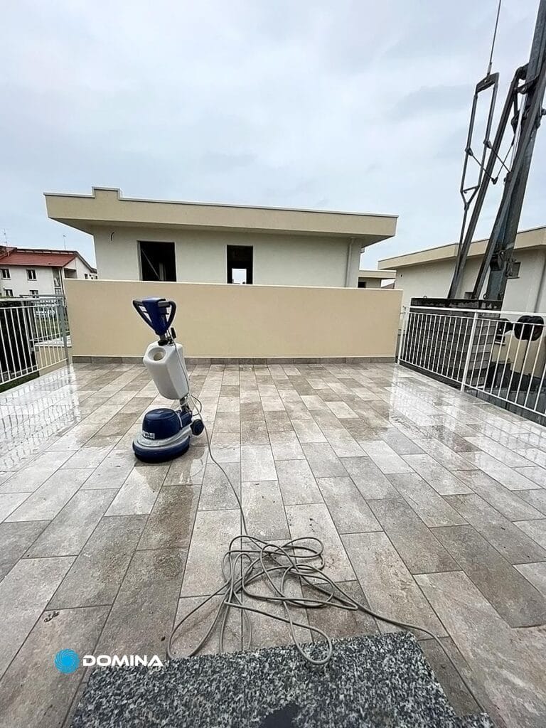 Una lucidatrice per pavimenti Pulizia fine cantiere Cadorago con un lungo cavo su un patio piastrellato sul tetto, circondato da ringhiere metalliche, sotto un cielo coperto.