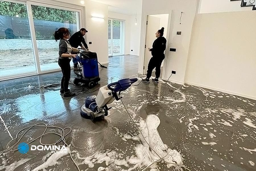 Tre persone eseguono una pulizia professionale del pavimento in una stanza con una macchina monospazzola professionale.