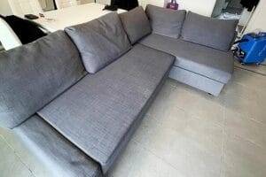 Un divano componibile grigio a forma di L dopo il lavaggio divani di Domina Pulizie.