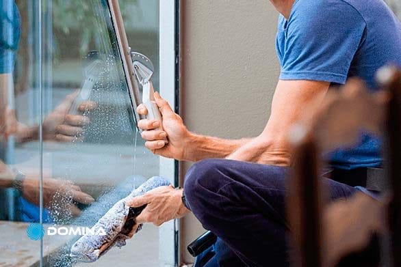 pulizie-vetrate-2 Una persona in maglietta blu esegue la pulizia professionale delle vetrate, utilizzando una spatola e un panno per pulire una finestra di vetro.