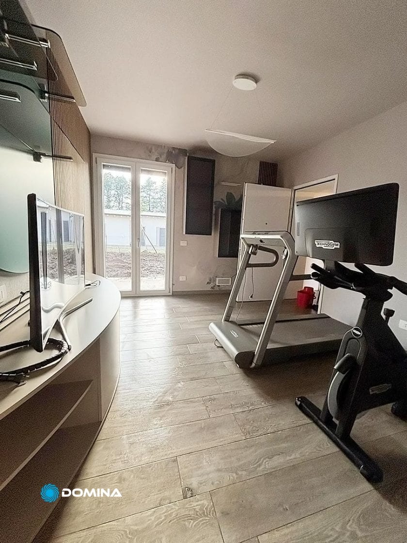 Una lussuosa palestra domestica dotata di tapis roulant e cyclette su un elegante pavimento in legno. Situata nel cuore del Centro di Milano, vanta un'ampia finestra che inonda lo spazio di luce naturale, incarnando comfort e stile.