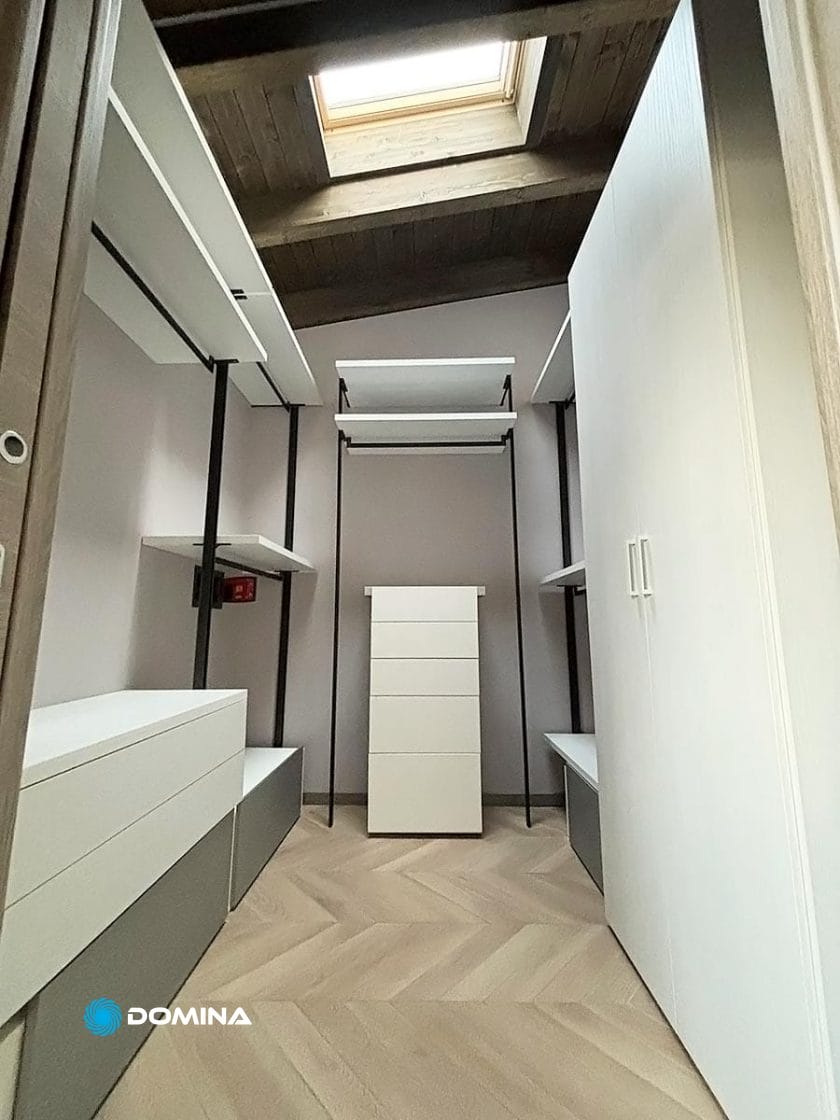 Una cabina armadio minimalista nel cuore del Centro di Milano vanta cassetti bianchi, ripiani e un guardaroba sotto un lucernario. Il pavimento presenta un motivo a spina di pesce, che fonde perfettamente eleganza e funzionalità per rinnnovare il lusso.