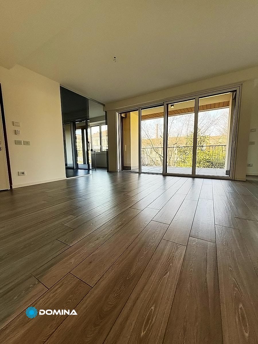 075-pulizie-appartamenti-city-life-milano-domina-pulizie-21022025 Ampia stanza vuota con pavimento in legno, grandi finestre e accesso a un balcone che lascia entrare molta luce naturale: perfetta per il tocco raffinato delle pulizie di lusso City Life Milano.